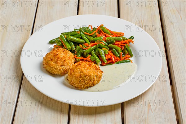 Meatballs in breading served with green bean and spicy carrot on wooden table