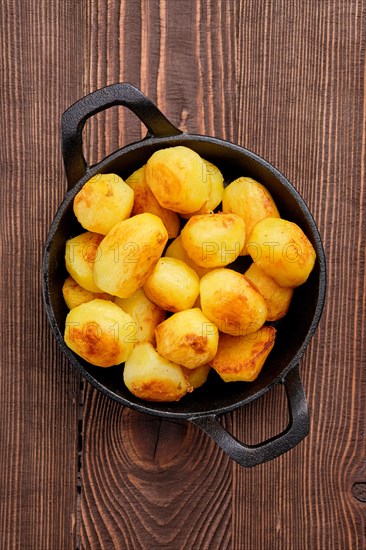 Top view of baked potato in cast iron skillet on natural wooden background