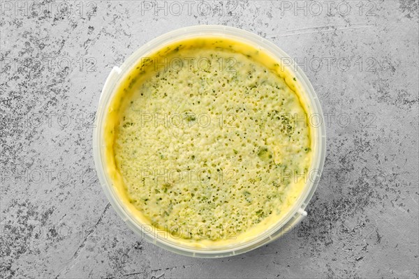 Top view of homemade soft cheese with herbs in plastic bowl