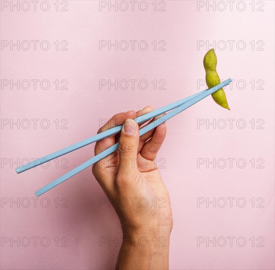 Hand holding chopsticks with edamame bean