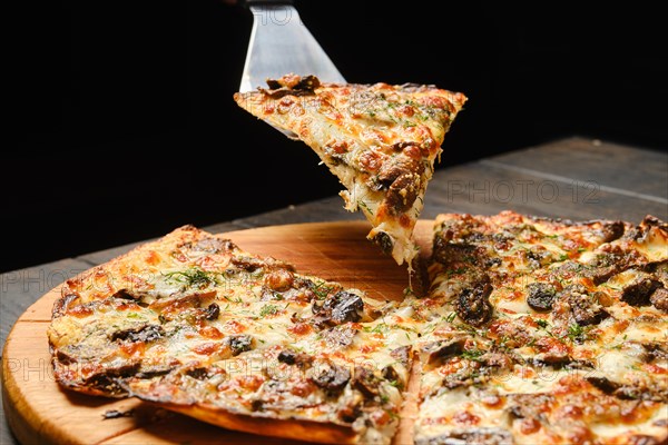 Lifting piece of thin dough pizza with mushroom on spatula