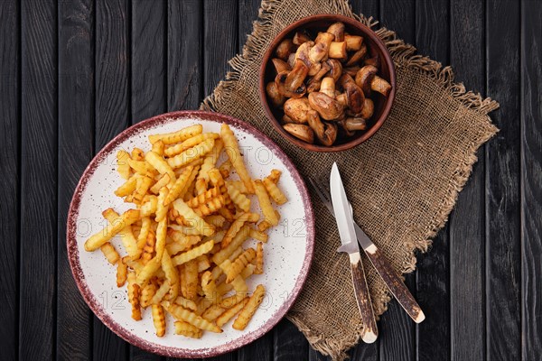 Fried crinkle cut american fries and roasted mushrooms on dark wooden table