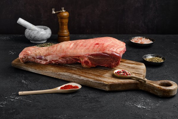 Raw half of turkey breast with bone and skin on dark background