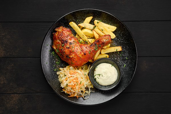 Top view of baked chicken leg with american fries and pickled cabbage on a plate