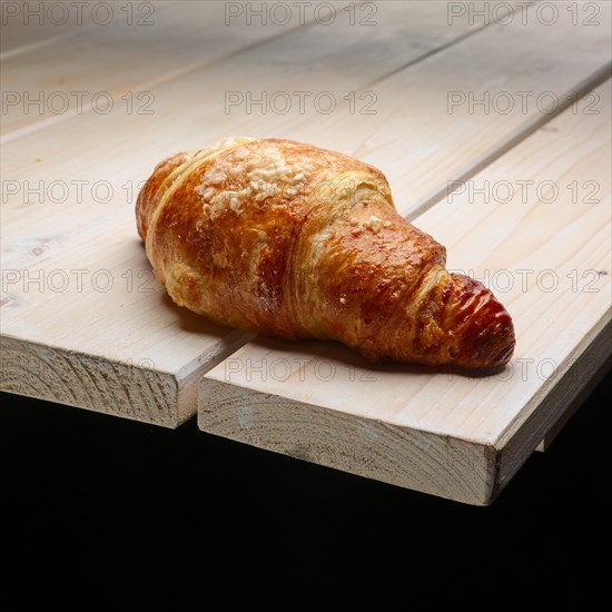 Fresh crisp croissant with powdered sugar on the corner of wooden table