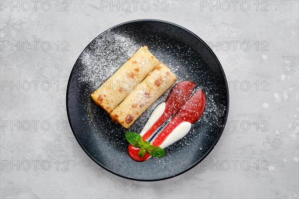 Top view of thin crepe stuffed with cottage cheese served with strawberry jam and sour cream