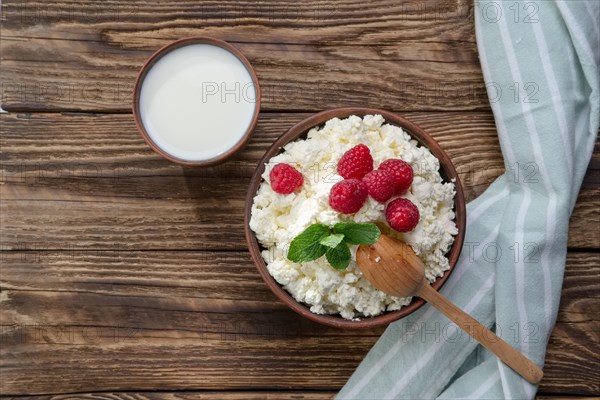 Fresh cottage cheese with raspberries and wooden spoon in clayware on wooden table