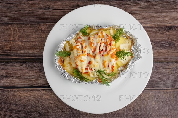 Top view of fried in foil sea fish and potato with paprika and cheese on wooden table