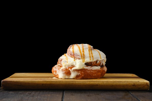 Cinnabon bun with caramel and icing on wooden serving board