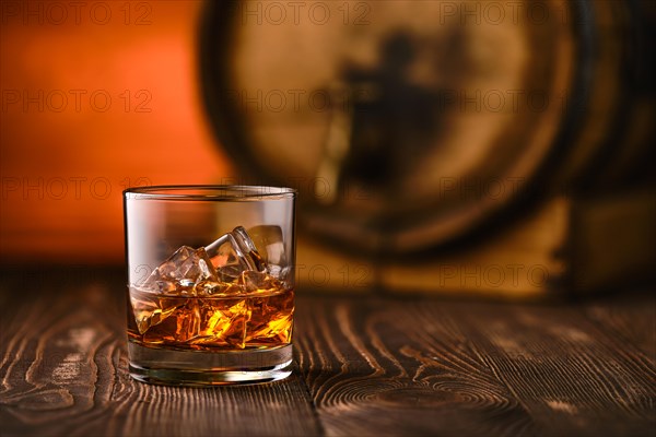 Glass of whisky with ice with barrel on background