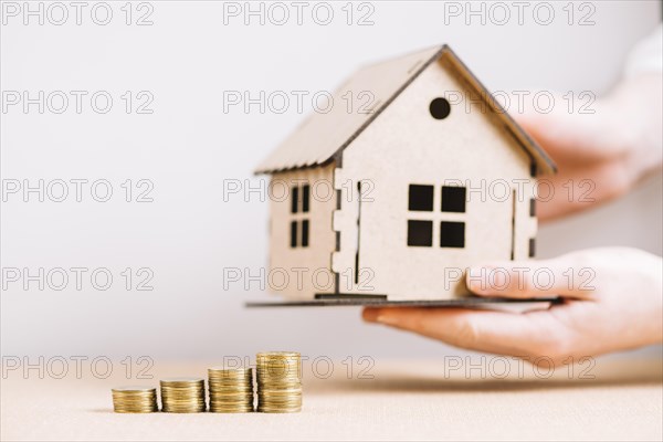 Crop hand holding house near coins