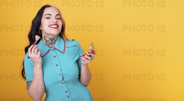 Attractive Woman Applying Face Powder over yellow Studio Background