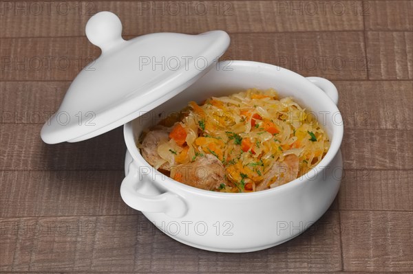 White bowl with homemade sausage and pickled cabbage baked in oven on wooden table