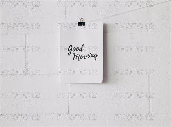 Good morning tag attach on string with bulldog paper clip against white wall