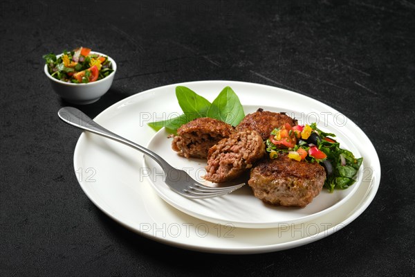 Fried veal meatballs on a plate with basil and tomato