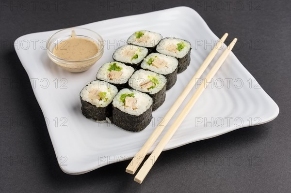 Chicken roll with nori and nut sauce on white plate near hashi