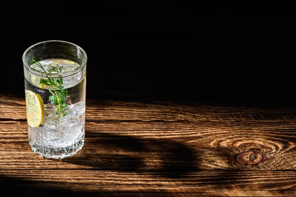 Carbonated cold water with ice and lemon dropping long shadow on wooden table