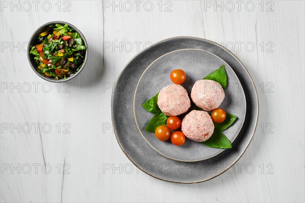 Top view of semifinished frozen veal meatballs on a plate with basil and tomato