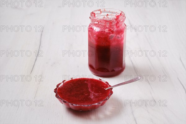 Jar and saucer with cherry jam on white wooden background