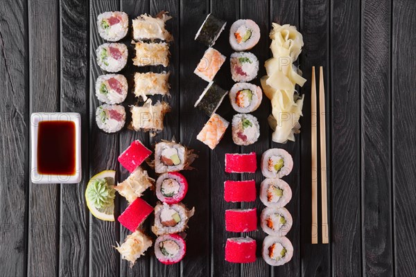 Large set of rolls with garnish and hashi on dark wooden plate