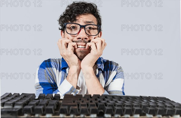 Nervous nerdy guy biting his nails in front of the keyboard