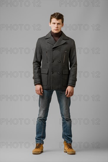 Full length portrait of handsome man in warm woolen coat posing in studio