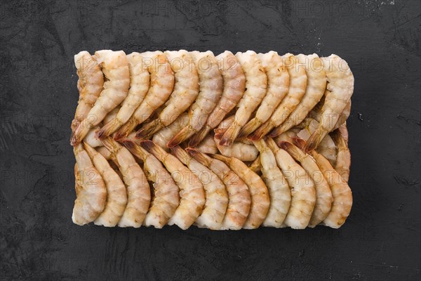 Overhead view of raw tiger shrimp frozen in large ice cube on black concrete background