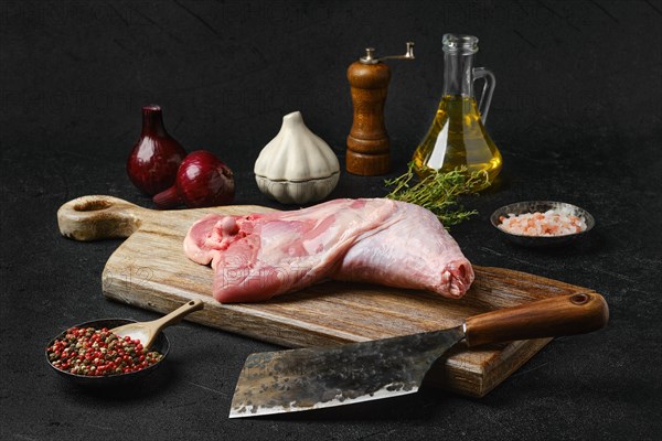 Raw turkey leg with skin on cutting board with cooking ingredients on black background