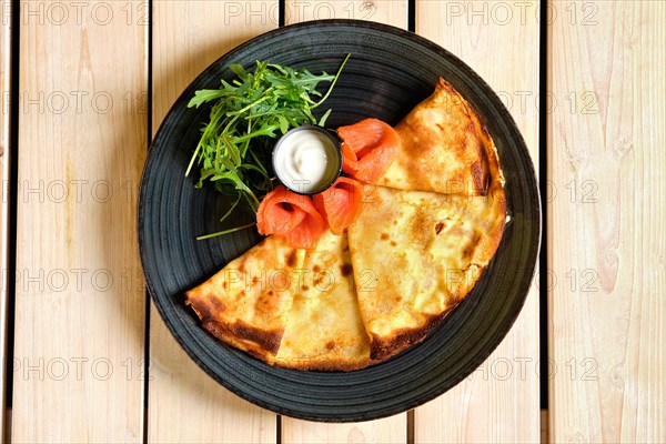 Overhead view of thin pancakes with salmon and sour cream