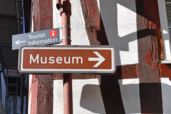 Direction signs leading to museum and tourist information in front of old traditional german half timbered house wall