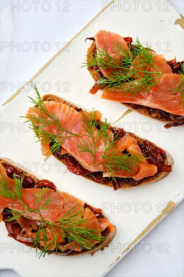 Top view of salmon sandwich with caramelized onion on wooden serving board