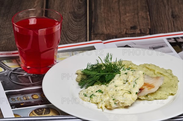 Fried fish and mashed potato with glass of fruit-drink on wooden table