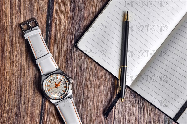 Top view of open blank notebook with pen and wrist watch on wooden table