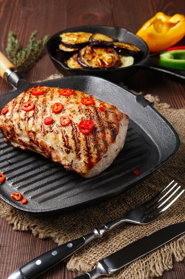 Grilled striploin on cast iron skillet and fried eggplant on wooden background