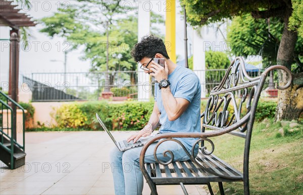 Man in a park working online with laptop and calling on cellphone. Freelancer man working with laptop while calling on the phone