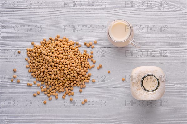 Top view of bottle and pitcher of soy milk on white wooden table