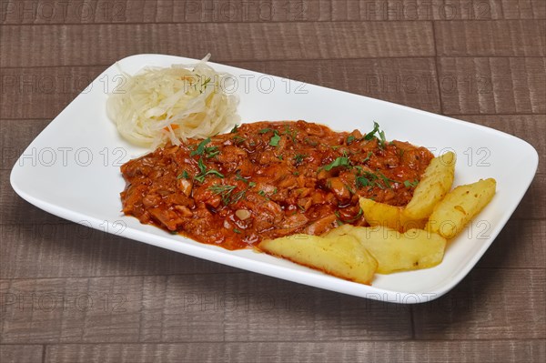 Beef goulash with potato wedges and pickled cabbage on wooden table