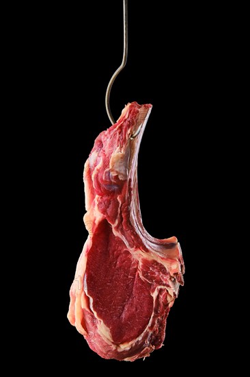 Beef ribeye steak bone-in on steel hook on black background