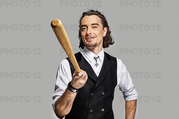 Dramatic man in white shirt and black vest with long curly hair holding baseball bat