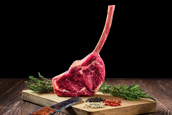 Raw juicy cowboy steak on wooden cutting board with spice