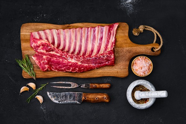 Fresh raw rack of lamb on wooden cutting board with herbs and seasoning