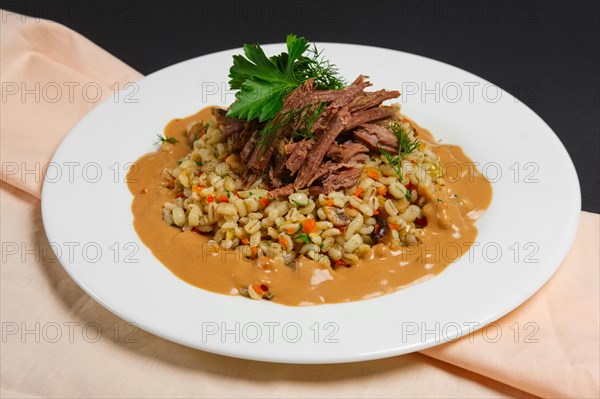 Plate with boiled beef and pearl barley on black background