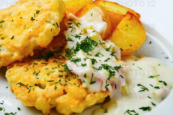 Close up view of ground chicken meat cutlet with fried potato wedges and creamy sauce with bacon on white wooden table