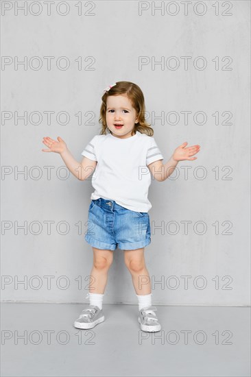 Two years old girl in white t-short and jeans shorts posing in studio