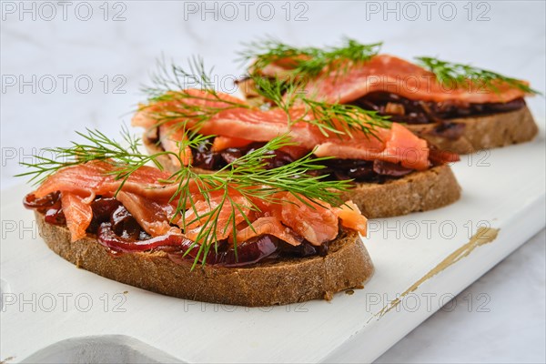 Closeup view of salmon sandwich with caramelized onion on wooden serving board