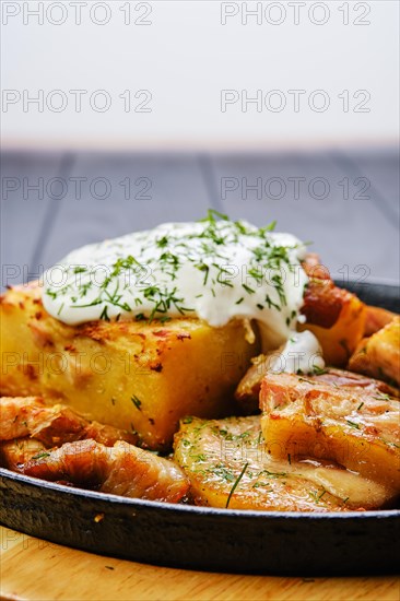 Close up view of potato casserole with fried pork mini belly slices on dark wooden table