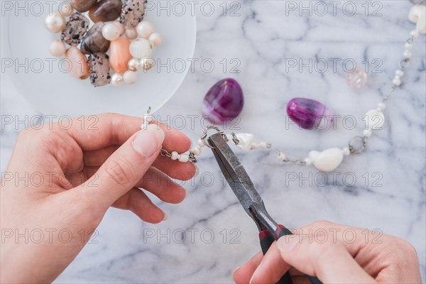 Close up woman s hand fixing bracelet with plier marble desk