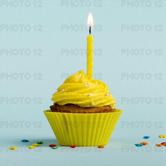 Yellow burning candles decorative muffins with colorful star sprinkles against blue backdrop. Resolution and high quality beautiful photo