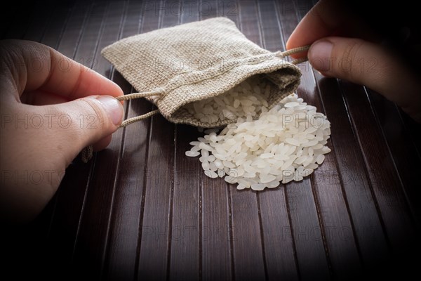 Hand holding straw pouch full of uncooked rice on a wooden background