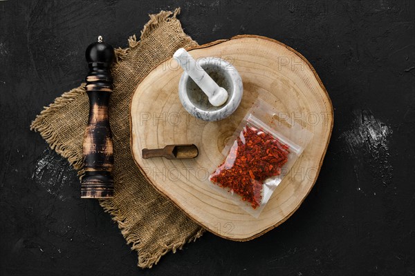 Wooden cross section with crushed paprika in plastic package and stone mortar and mill